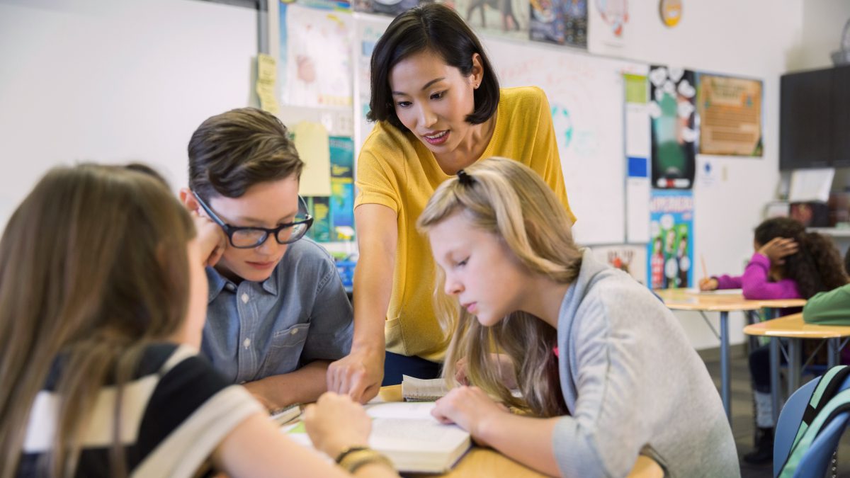 Female teacher with two students reading book